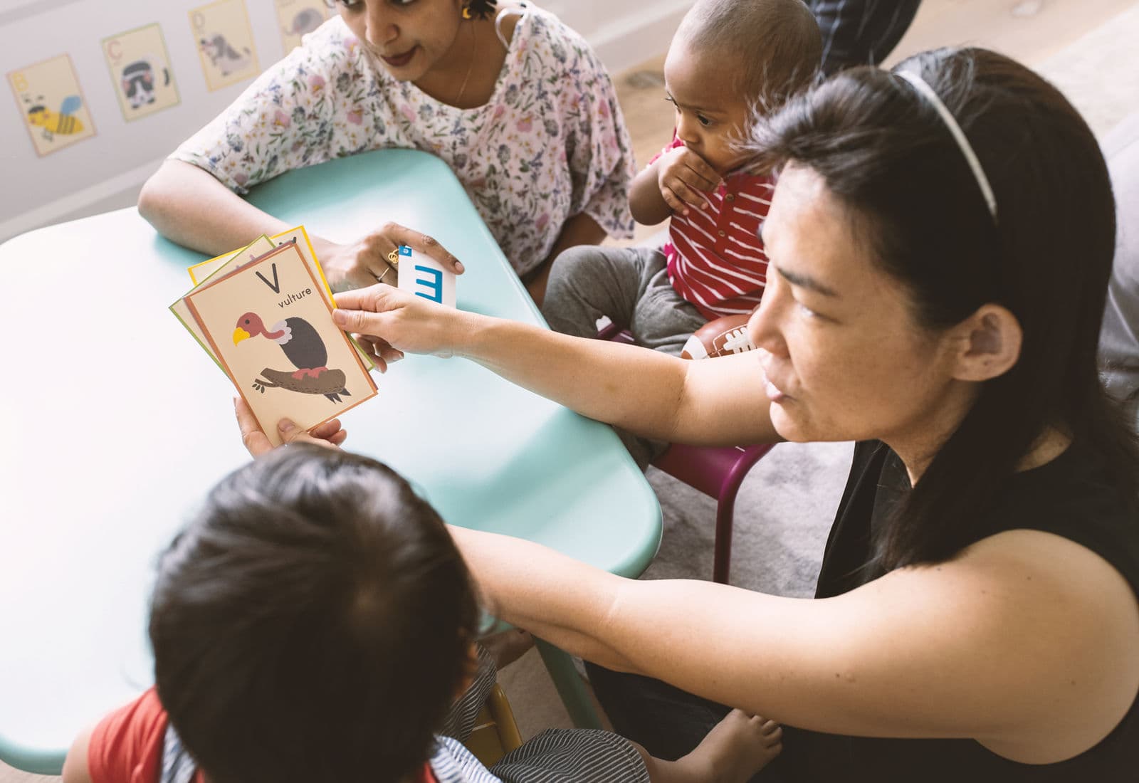 Educators and children sharing alphabet cards at a low table